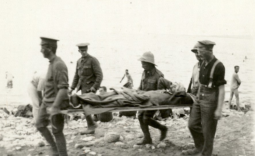 A wounded soldier is stretchered along Ocean Beach as men bath in the shallows.